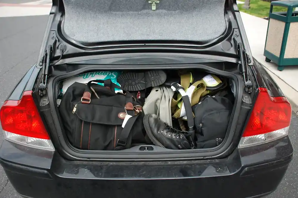 Rear view of a sedan with its trunk open, holding duffel bags and a shoulder bag